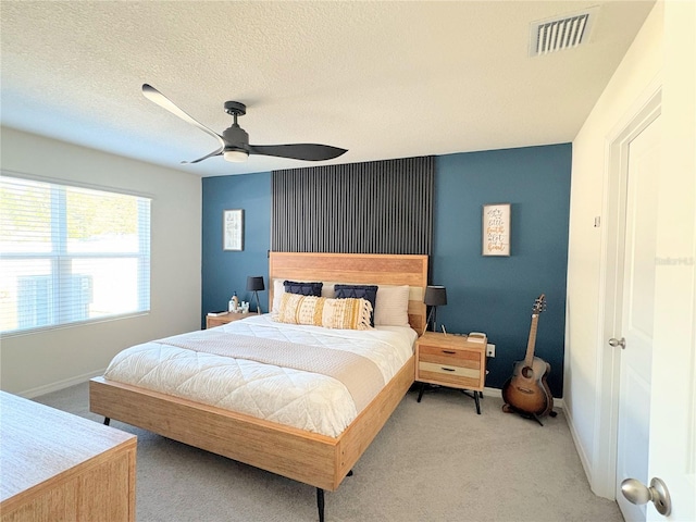 bedroom with ceiling fan, light colored carpet, and a textured ceiling