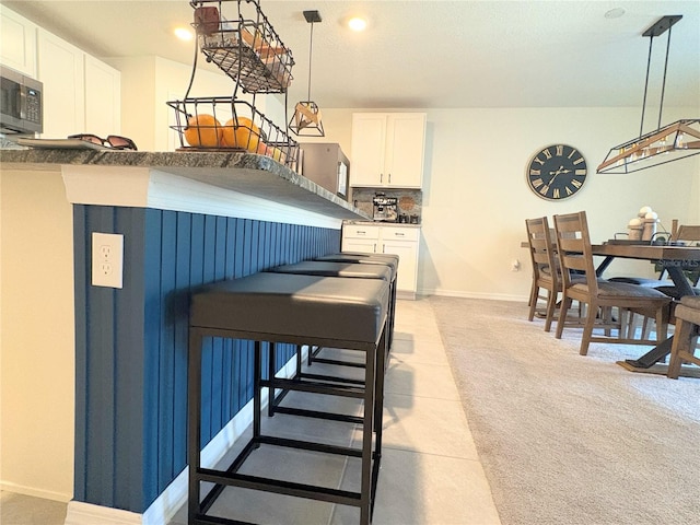 kitchen with white cabinetry, light colored carpet, a breakfast bar area, and hanging light fixtures