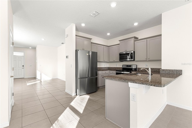 kitchen with dark stone counters, a kitchen breakfast bar, light tile patterned floors, kitchen peninsula, and stainless steel appliances