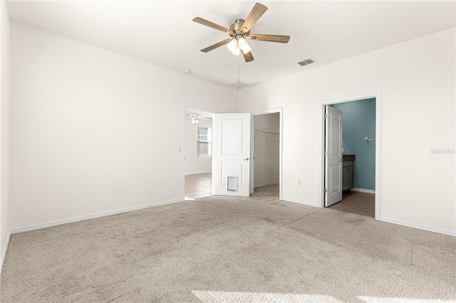 unfurnished bedroom with a walk in closet, ceiling fan, connected bathroom, light colored carpet, and a closet