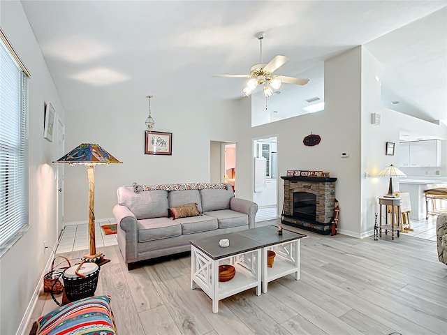 living room with ceiling fan, light hardwood / wood-style floors, a fireplace, and high vaulted ceiling