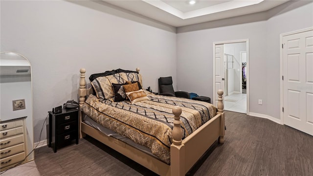 bedroom with connected bathroom, a tray ceiling, and dark hardwood / wood-style floors