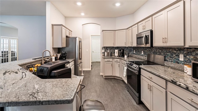 kitchen with light stone countertops, appliances with stainless steel finishes, dark hardwood / wood-style flooring, and decorative backsplash