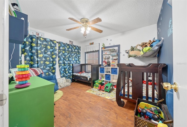 bedroom with a crib, ceiling fan, hardwood / wood-style floors, and a textured ceiling