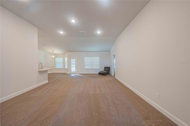 unfurnished living room with a notable chandelier, lofted ceiling, and carpet floors