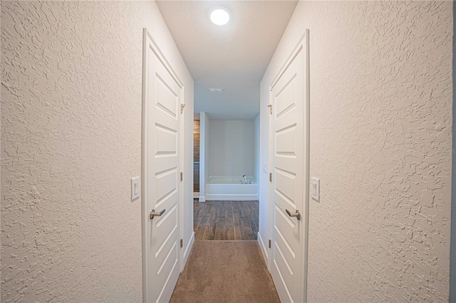 hall with dark carpet and a textured ceiling