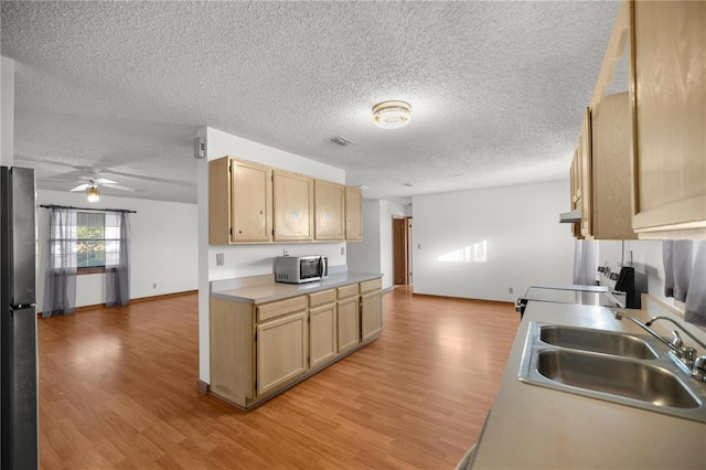 kitchen with light brown cabinets, range, sink, and stainless steel refrigerator