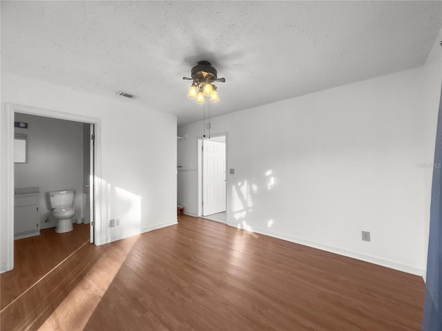 unfurnished bedroom featuring a textured ceiling, ensuite bath, ceiling fan, and dark wood-type flooring