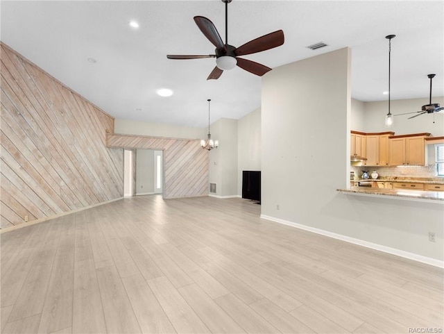 unfurnished living room featuring wooden walls, light hardwood / wood-style flooring, and ceiling fan with notable chandelier