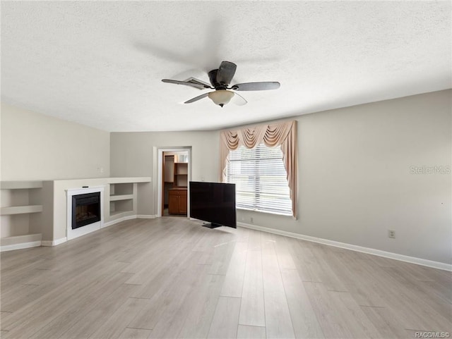 unfurnished living room with built in shelves, ceiling fan, light hardwood / wood-style flooring, and a textured ceiling