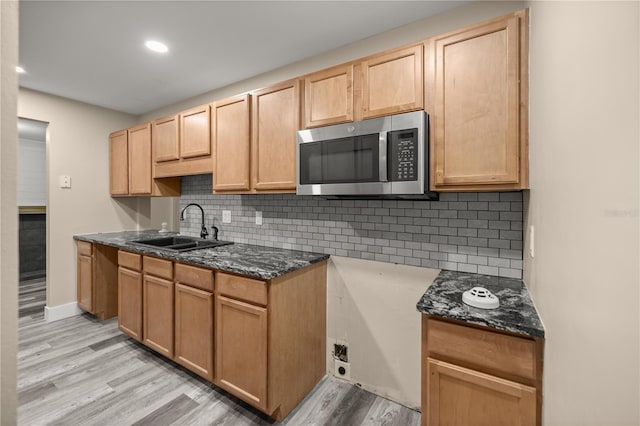 kitchen with backsplash, dark stone countertops, sink, and light hardwood / wood-style flooring