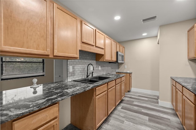 kitchen with light brown cabinetry, sink, dark stone counters, and light wood-type flooring