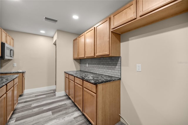 kitchen with dark stone countertops, light wood-type flooring, and backsplash