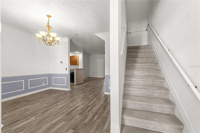 stairs featuring crown molding, hardwood / wood-style floors, ceiling fan with notable chandelier, and a textured ceiling