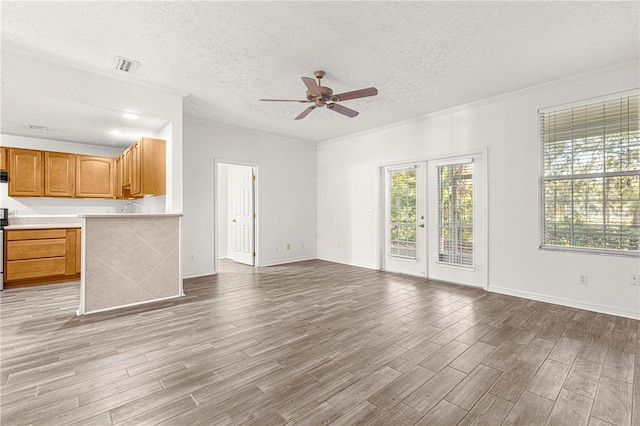 unfurnished living room featuring ceiling fan, ornamental molding, a textured ceiling, and french doors