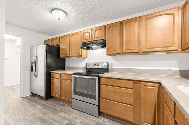 kitchen with light wood-type flooring, a textured ceiling, and appliances with stainless steel finishes