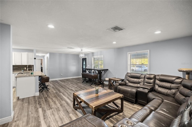 living room with a textured ceiling, sink, and light hardwood / wood-style flooring