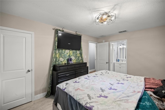 bedroom with ensuite bath, a textured ceiling, and light wood-type flooring