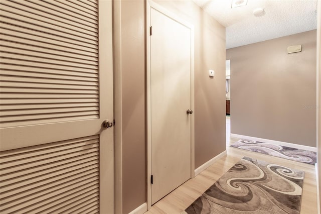 hall with a textured ceiling and light hardwood / wood-style flooring