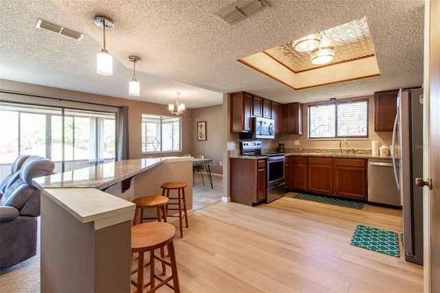 kitchen with kitchen peninsula, appliances with stainless steel finishes, decorative light fixtures, a chandelier, and a breakfast bar area