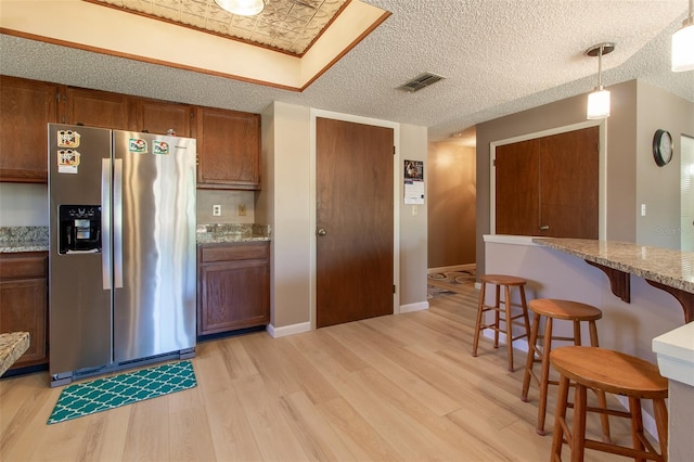 kitchen with a kitchen breakfast bar, light stone counters, decorative light fixtures, light hardwood / wood-style flooring, and stainless steel fridge with ice dispenser