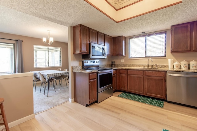 kitchen featuring sink, hanging light fixtures, light stone counters, light hardwood / wood-style floors, and appliances with stainless steel finishes