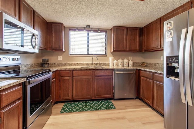 kitchen featuring light stone counters, sink, a textured ceiling, and appliances with stainless steel finishes