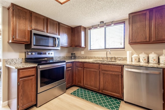 kitchen with sink, light wood-type flooring, a textured ceiling, light stone counters, and stainless steel appliances