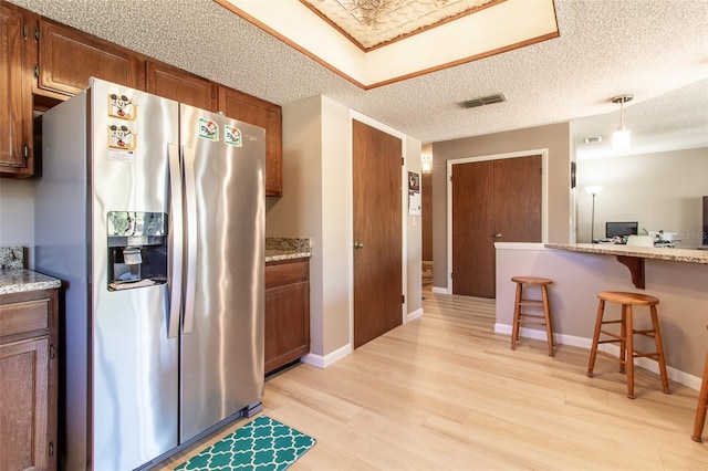 kitchen with light stone countertops, light hardwood / wood-style flooring, stainless steel fridge, decorative light fixtures, and a breakfast bar area