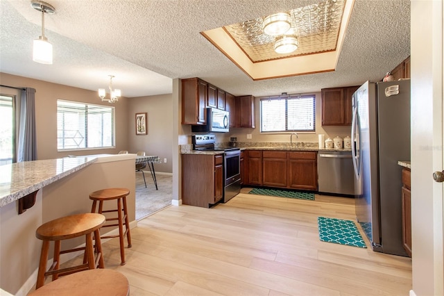 kitchen with hanging light fixtures, light hardwood / wood-style flooring, appliances with stainless steel finishes, a notable chandelier, and a kitchen bar