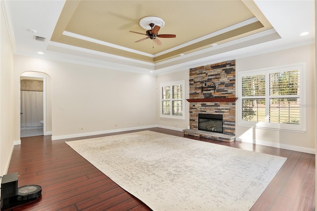 unfurnished living room with ceiling fan, ornamental molding, a raised ceiling, and a stone fireplace