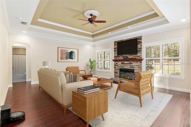 living room with a raised ceiling, ceiling fan, a fireplace, and ornamental molding