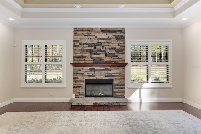 unfurnished living room with ornamental molding, a raised ceiling, dark hardwood / wood-style floors, and a stone fireplace