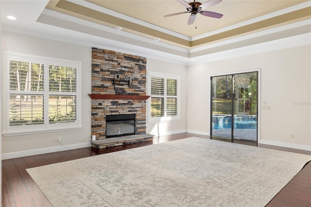 unfurnished living room featuring a raised ceiling, ceiling fan, a stone fireplace, and ornamental molding