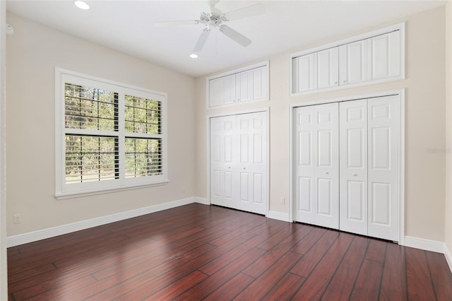 unfurnished bedroom with ceiling fan, multiple closets, and dark wood-type flooring