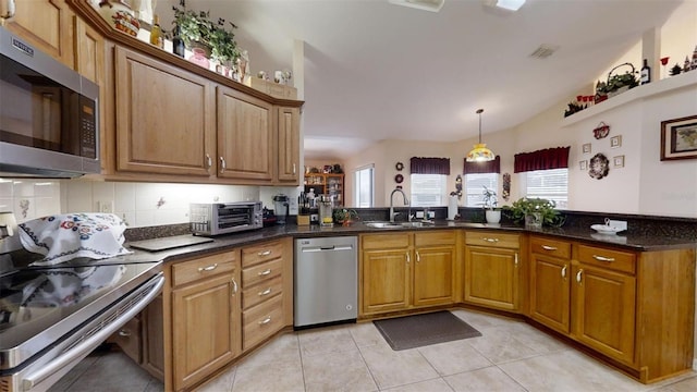 kitchen featuring sink, light tile patterned flooring, dark stone countertops, kitchen peninsula, and appliances with stainless steel finishes