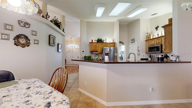 kitchen featuring kitchen peninsula, stainless steel appliances, light tile patterned flooring, and a skylight