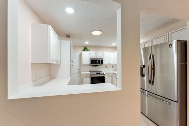 kitchen featuring kitchen peninsula, a textured ceiling, stainless steel appliances, and white cabinetry