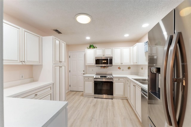 kitchen featuring white cabinets, sink, a textured ceiling, light hardwood / wood-style floors, and stainless steel appliances