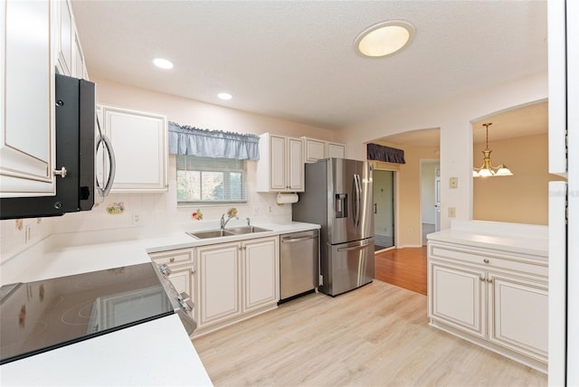 kitchen featuring sink, stainless steel appliances, a notable chandelier, decorative light fixtures, and light wood-type flooring