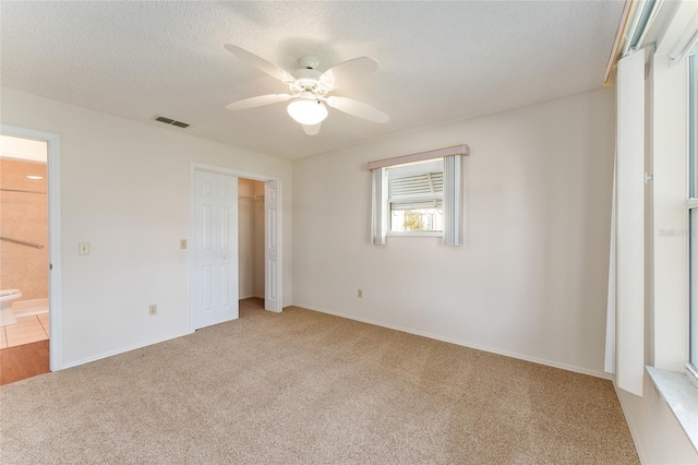 unfurnished bedroom with light carpet, a textured ceiling, ensuite bath, and ceiling fan