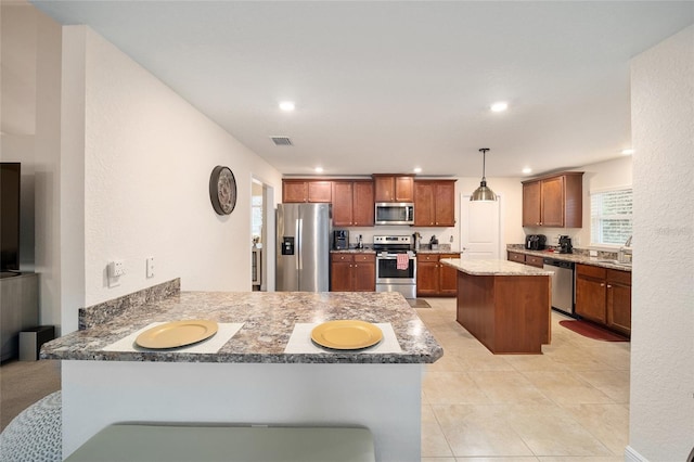 kitchen featuring light stone counters, kitchen peninsula, hanging light fixtures, appliances with stainless steel finishes, and sink