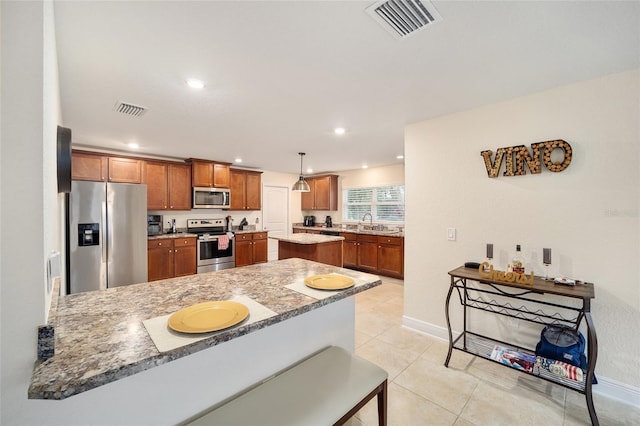 kitchen with stainless steel appliances, hanging light fixtures, kitchen peninsula, light stone counters, and light tile patterned flooring