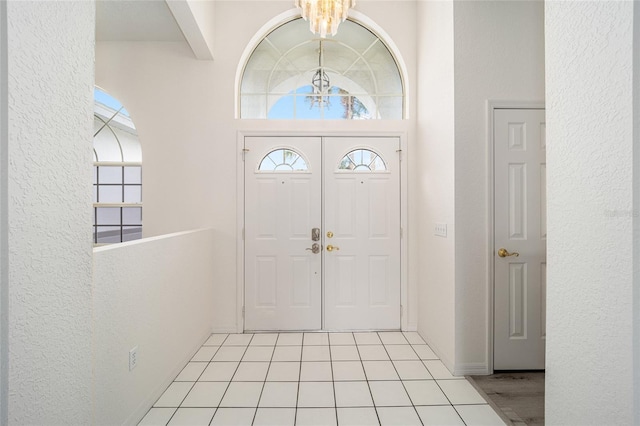 entryway featuring a towering ceiling, light tile patterned floors, and an inviting chandelier