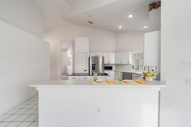 kitchen featuring kitchen peninsula, stainless steel appliances, vaulted ceiling, light tile patterned floors, and white cabinets