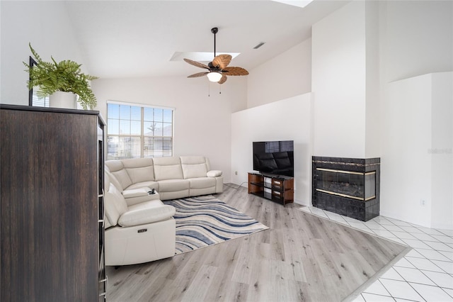 living room featuring ceiling fan, a multi sided fireplace, light wood-type flooring, and high vaulted ceiling