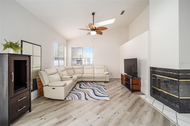 living room with a tile fireplace, ceiling fan, light hardwood / wood-style flooring, and lofted ceiling