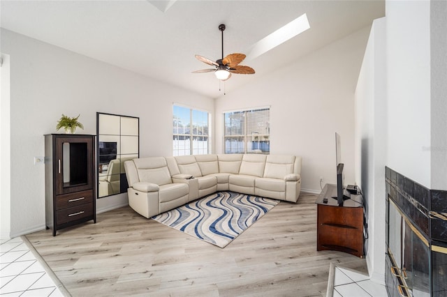 living room featuring lofted ceiling with skylight, ceiling fan, and light wood-type flooring