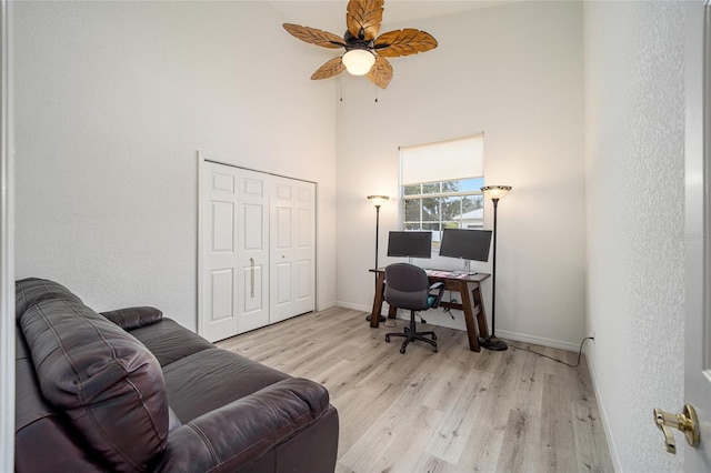 office space featuring ceiling fan, a towering ceiling, and light hardwood / wood-style flooring