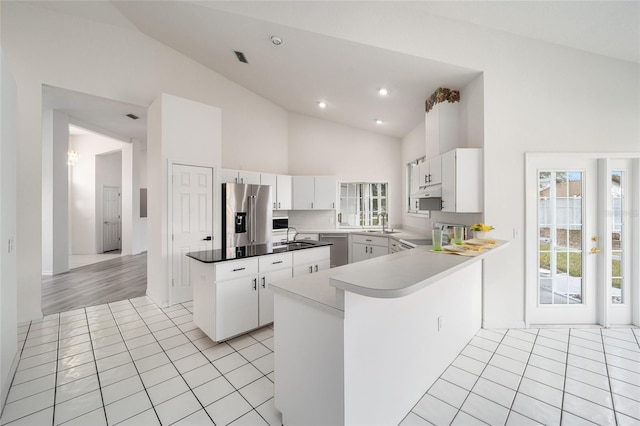 kitchen with high vaulted ceiling, a peninsula, a kitchen island, a sink, and stainless steel appliances